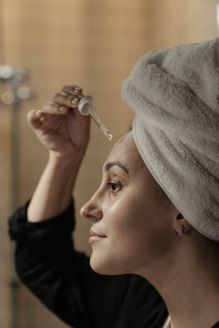 Başında havlu, evde yüzüne serum damlatmaya hazırlanan bir kadın